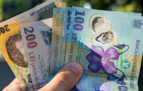 Mână ținând bani românești. Bancnote românești de 100 și 200 de lei ținute în mână