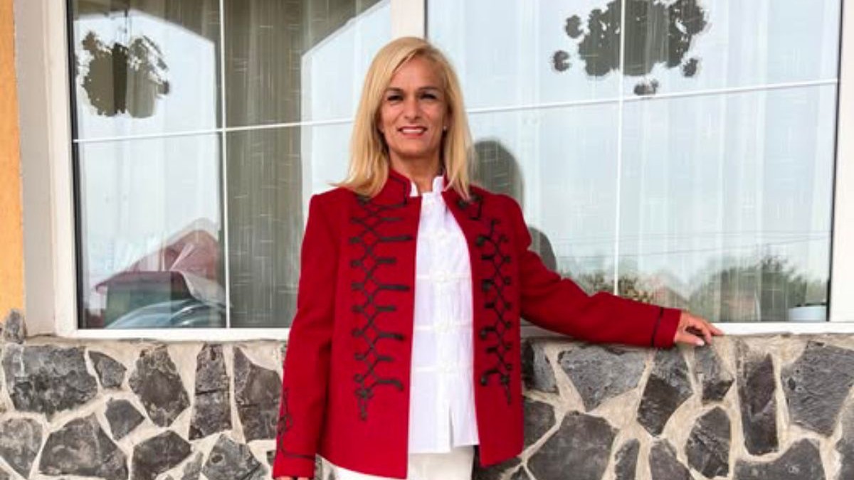 Campioana Judit Palecian, in tunica rosie cu model negru si o camasa alba, in fata unei case