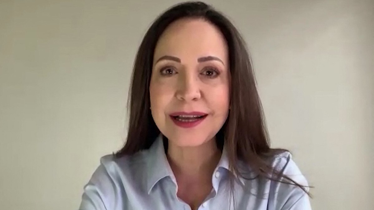 Maria Corina Machado in camasa albastra, cu parul lung, zambeste larg la camera