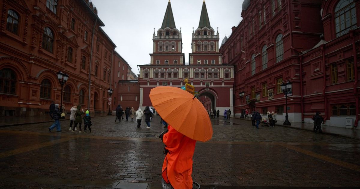 O femeie stă în ploaie cu umbrela desfăcută la Poarta Învierii din Moscova, joi, 11 decembrie 2025