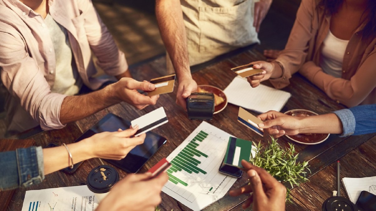 Mâini, carduri de credit, prieteni într-o cafenea, efectuând o plată sau o tranzacție bancară la un terminal POS.