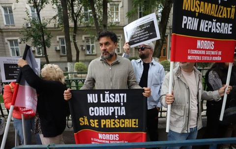 Mai mulți protestatari care țin bannere și pancarte cu mesaje împotriva corupției în fața DNA