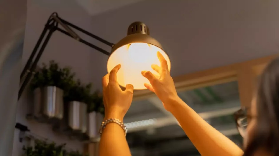 O femeie înșurubează un bec cu mâinile într-o veioză și se vede lumina. Foto: Shutterstock