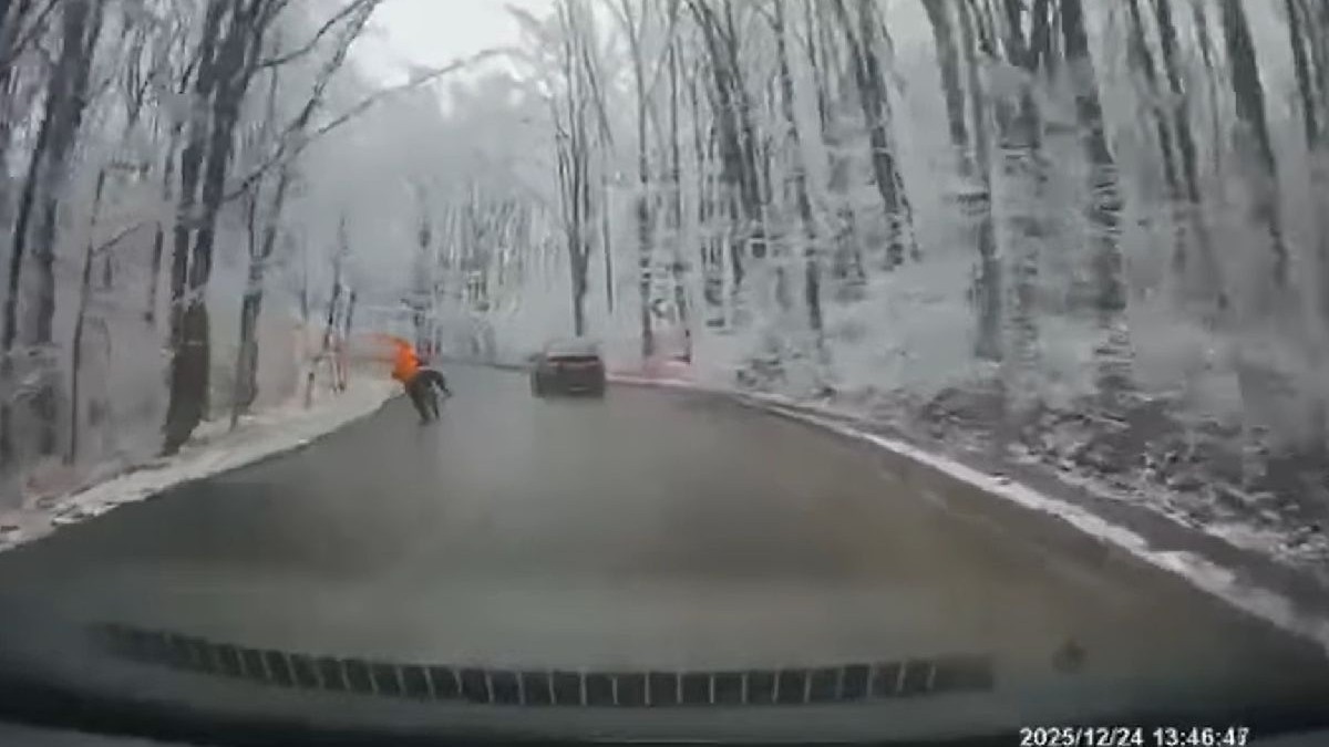 Fotogarfia arată un motocilist care depășește o mașină pe un carosabil umed, într-o pădure înzăpezătă.