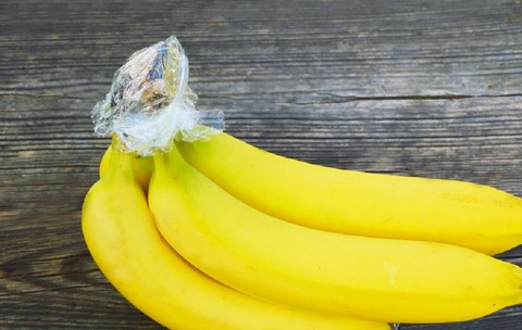 Banane galbene cu cotoarele înfășurate în folie din plastic, pe o masă din lemn.