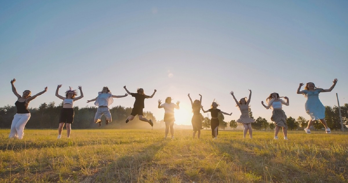 Când începe vacanța de vară 2026 - Mai mulți tineri sar de bucurie aer pe un câmp la apus