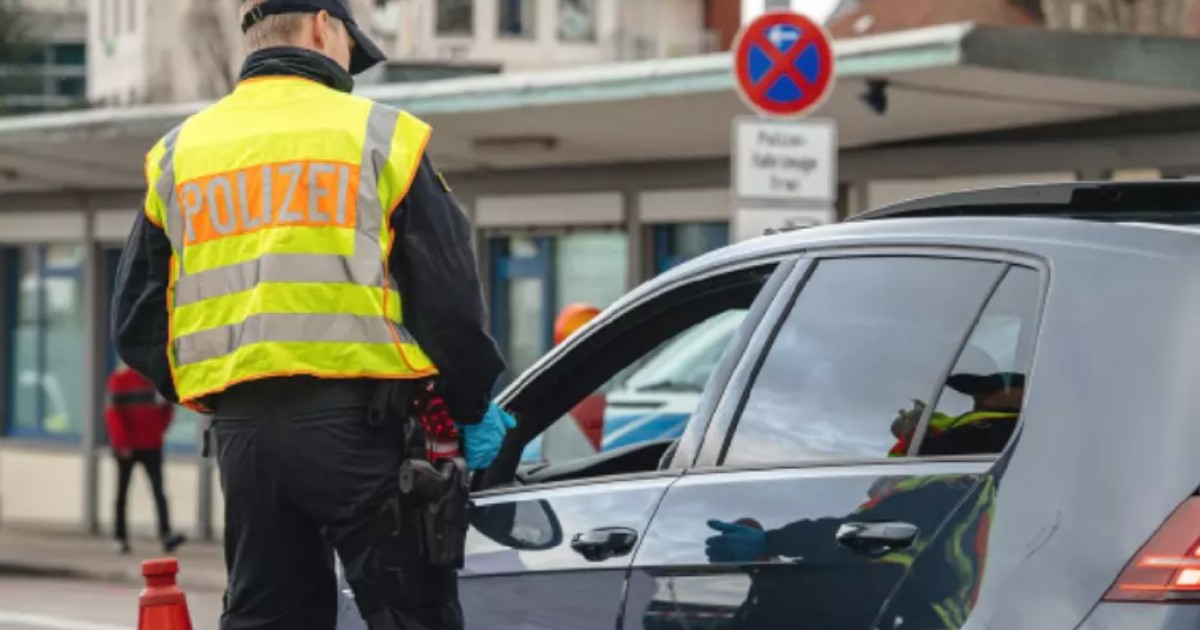 Un polițist care poartă vestă reflectorizantă pe care scrie Polizei. Acesta a oprit un șofer cu mașină neagră.