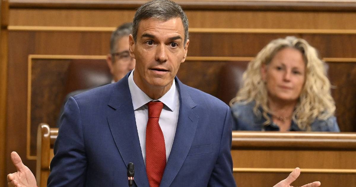 Premierul Pedro Sanchez în timpul unui discurs, e îmbrăcat în costum albastru și deschide larg mâinile penytru a expica ceva