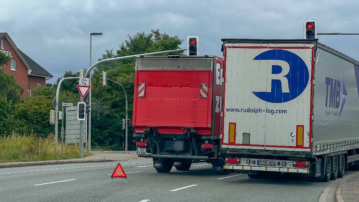 Un camion roșu și unul alb, unul lîngă altul, pe șosea