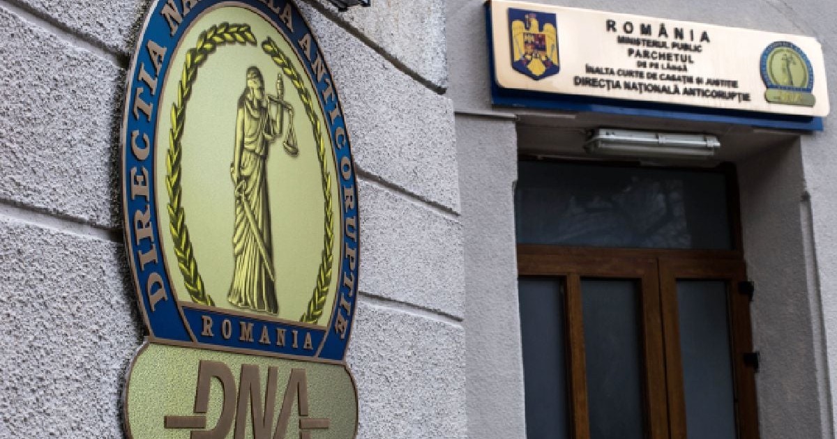 Imaginea surprinde intrarea în sediul Direcției Naționale Anticorupție (DNA). Sigla DNA: În prim-plan, pe peretele din stânga, se află o emblemă mare, circulară, cu inscripția "Direcția Națională Anticorupție - România" și acronimul "DNA" dedesubt.