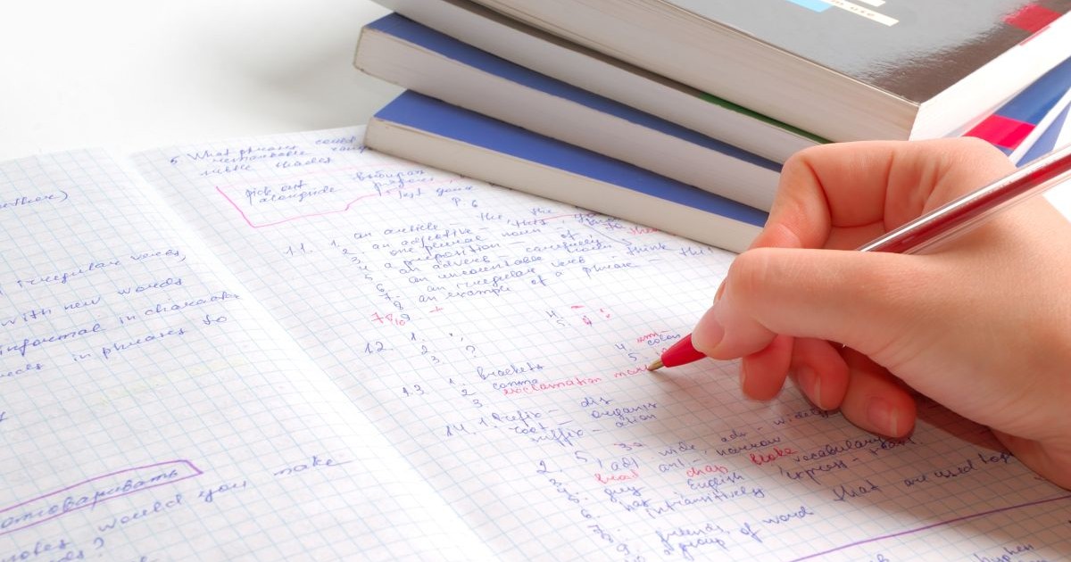 Un profesor corectează cu pixul roșu tema unui elev făcută pe un caiet