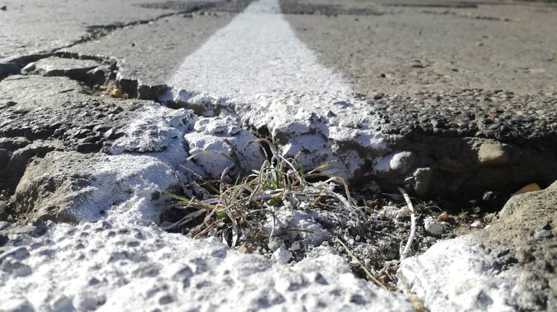 Se întâmplă în România! Au trasat marcaje pe un drum plin de gropi! "Dorel" a dat cu vopsea inclusiv peste iarba crescută în "craterele" din șosea