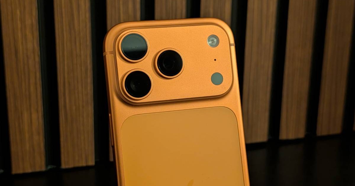 Platoul camerei foto a lui iPhone 17 Pro, de culoare portocalie, pe un fundal de lemn.