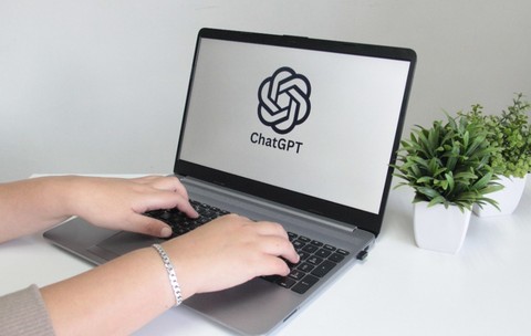 O femeie care scrie pe un laptop. Pe ecran este accesat ChatGPT