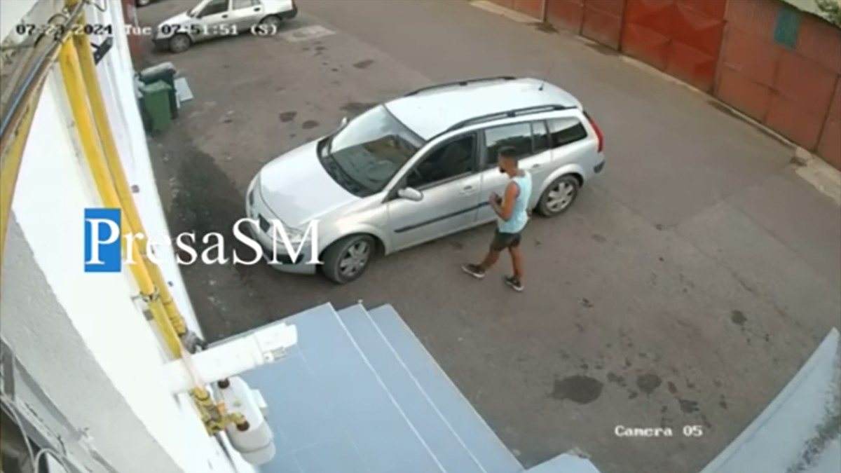 Un bărbat în tricou este suprins pe camerele de supraveghere când se uită la mașina pe care a furat-o ulterior din fața restaurantului
