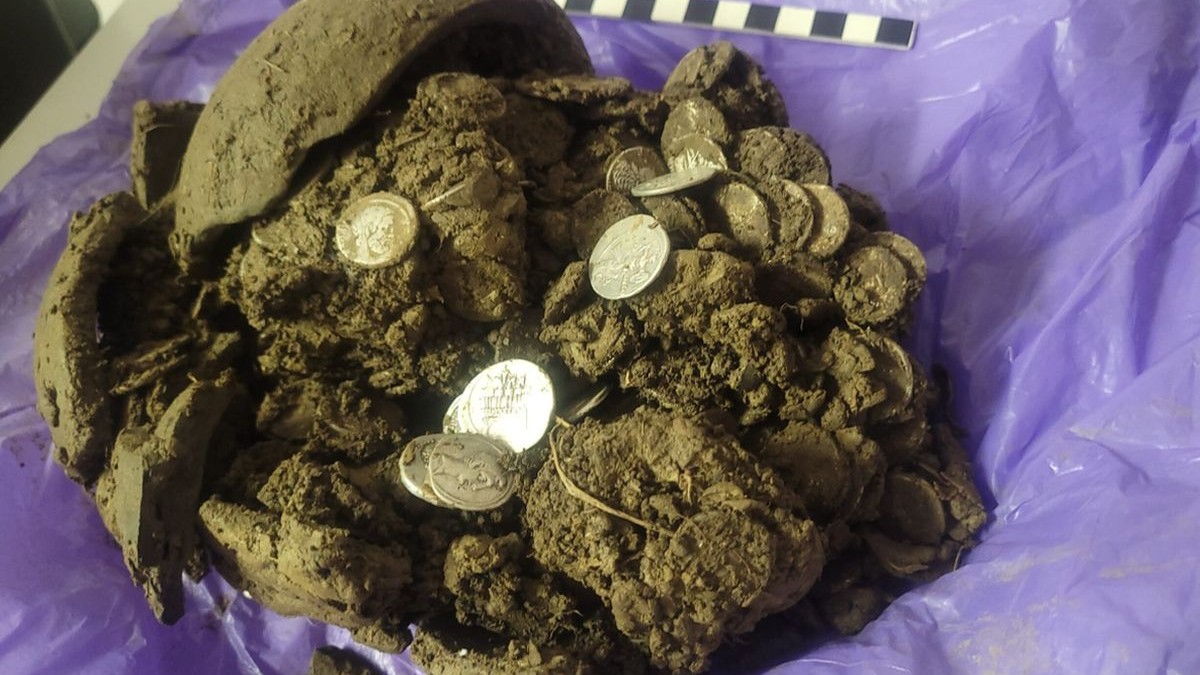 O bucată de pământ în care sunt câteva monede, pusă pe o pungă de plastic mov. Este un tezaur roman descoperit într-o pădure din Făgetu, comuna Gura Vitioarei, județul Prahova, 15 februarie 2026