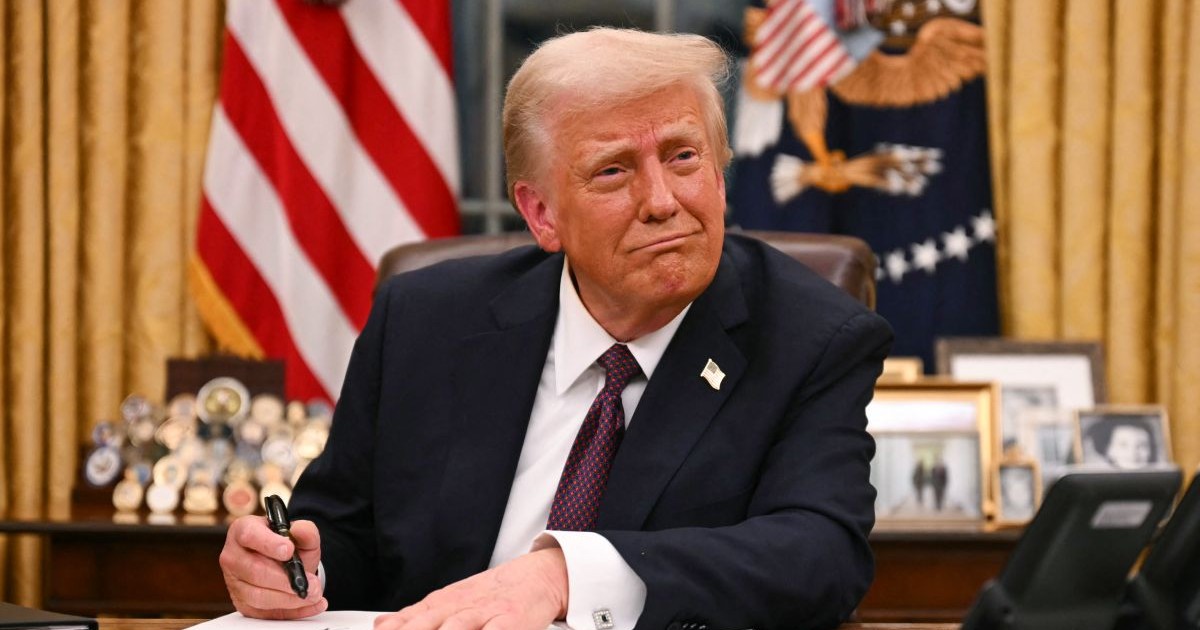 Donald Trump, îmbrăcat în costum, în timp ce stă la Biroul Oval, la Casa Albă, și semnează un document, în ianuarie 2025