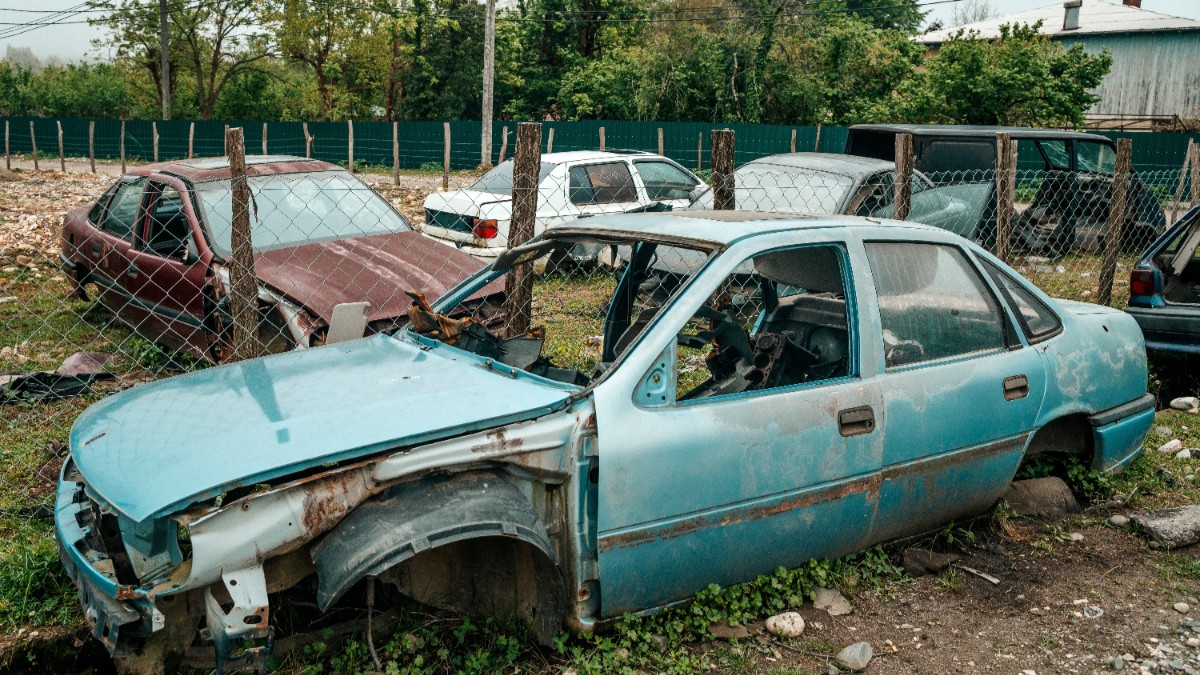 Mai multe mașini vechi, cu caroseria ruginită, care stau într-un parc auto