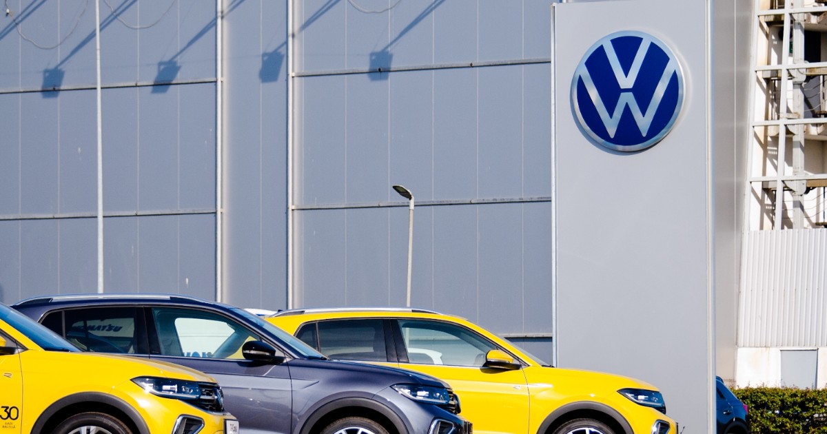 Mașini Volkswagen noi pe stradă, cu un zid gri în fundal.