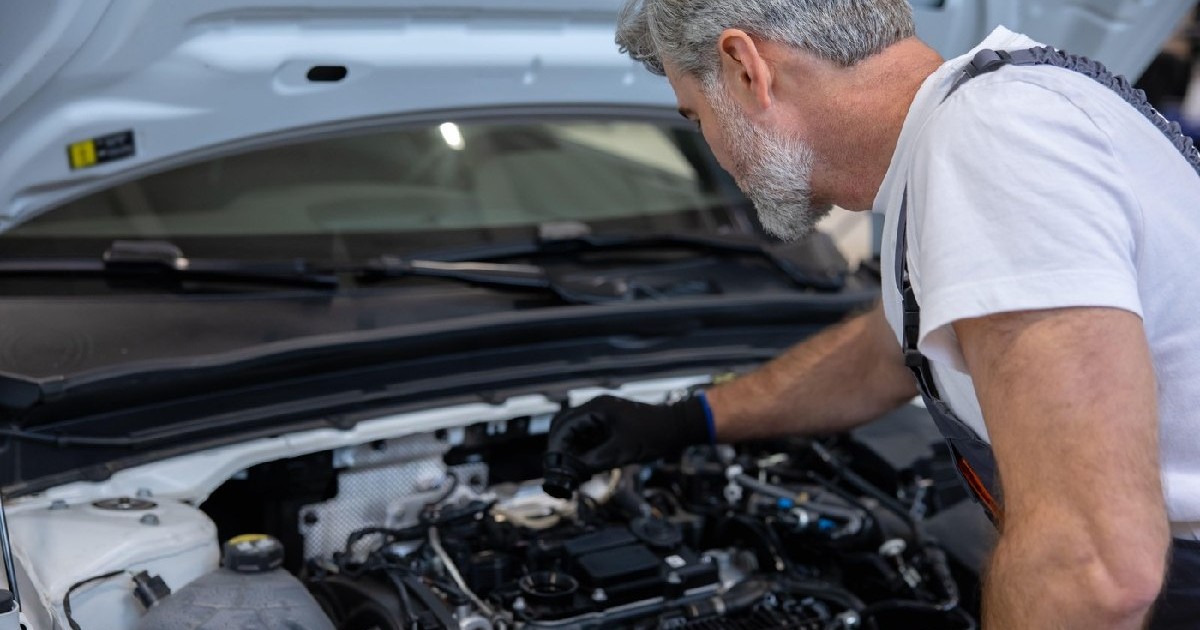 Mecanic verificând nivelul uleiului cu joja la motor, cu capota deschisă, într-un service auto.