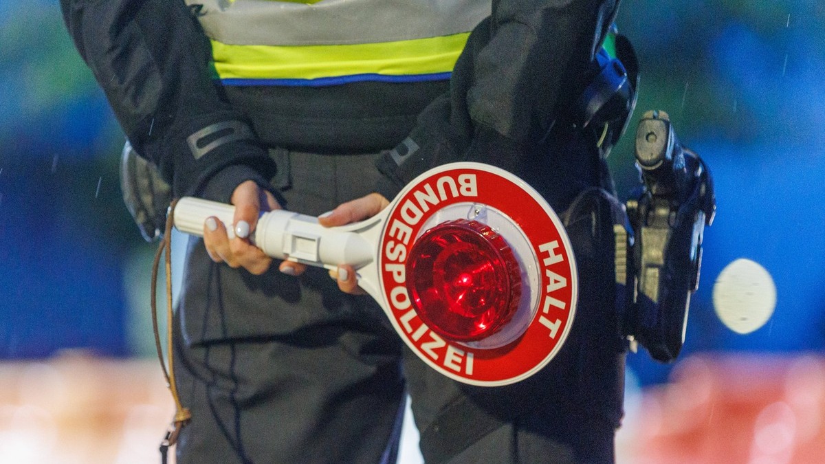 Polițist de frontieră german care ține în mână un semn pe care scrie STOP