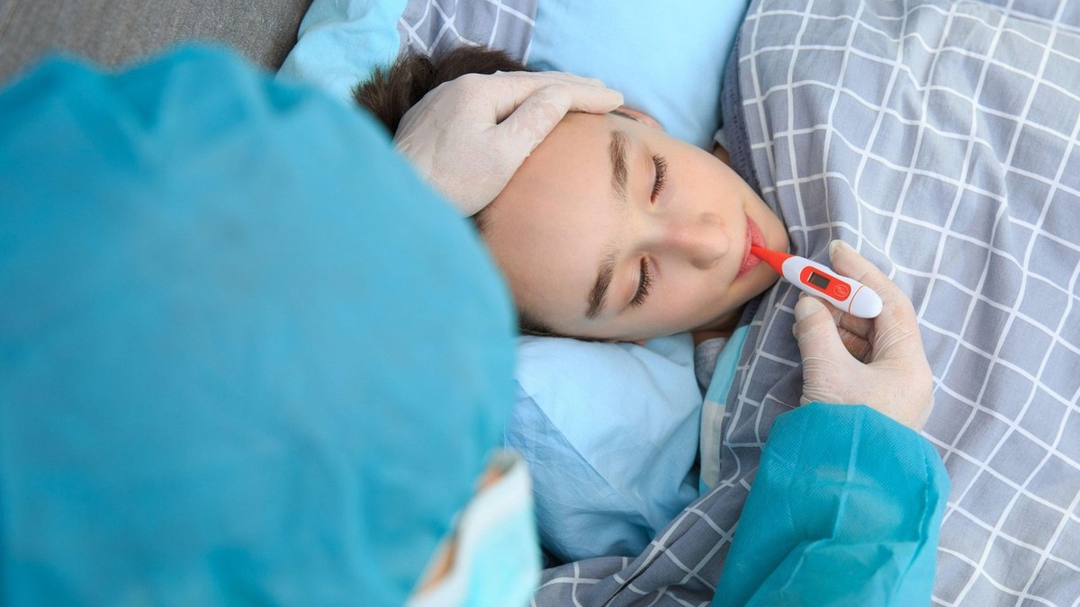 Un băiat bolnav stă întins pe pat și i se ia temperatura cu un termometru. În România a fost declarată stare de urgență epidemiologică din cauza gripei