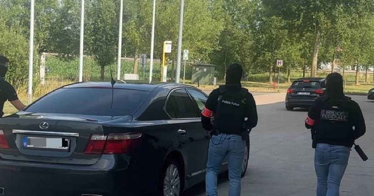 Trei indivizi mascați, îmbrăcați în hanorace negre cu glugă și blugi, unul dintre ei ținând o armă, se apropie de un Lexus oprit pe o stradă
