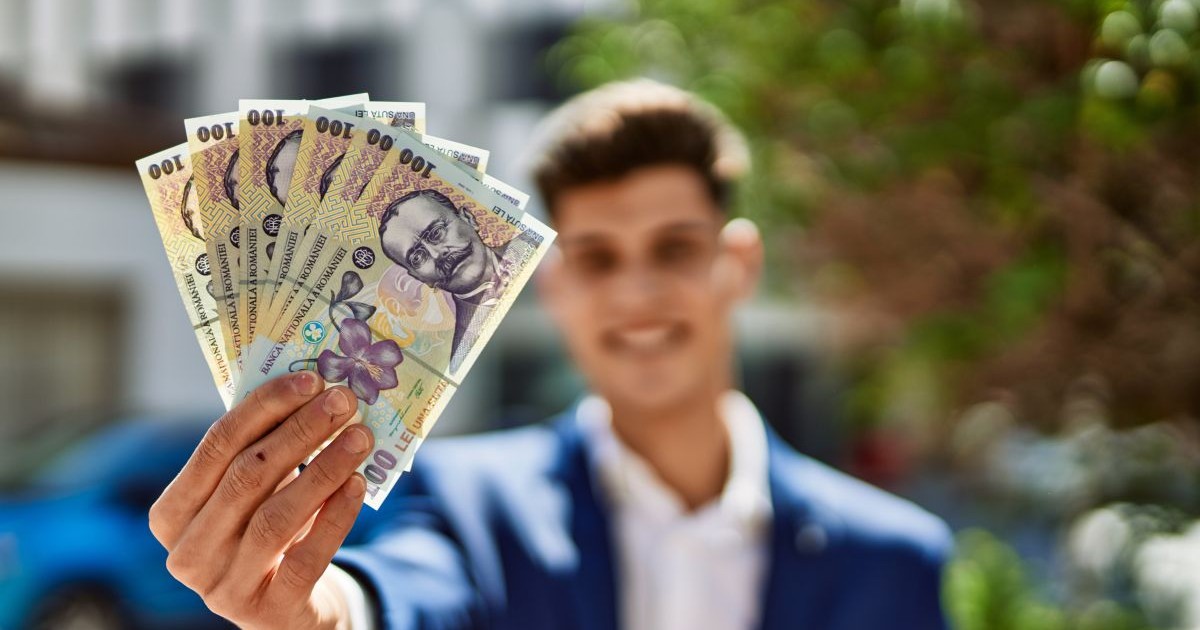 Un bărbat îmbrăcat la costum și cu fața blurată ține în mână mai multe bancnote de 100 de lei și le arată