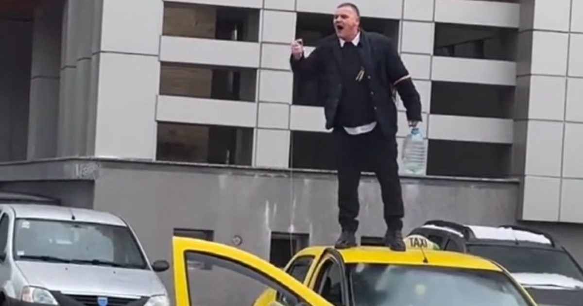 Taximetristul din Suceava, îmbrăcat în haine de culoare închisă, urcat pe plafonul taxiului de culoare galbenă