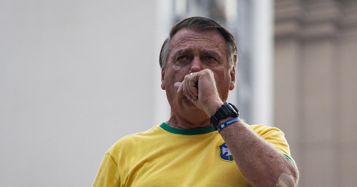Îmbrăcat cu un tricou galben al naționalei de fotbal a Braziliei, Jair Bolsonaro duce la gură mâna stângă cu pumnul strâns, septembrie 2024