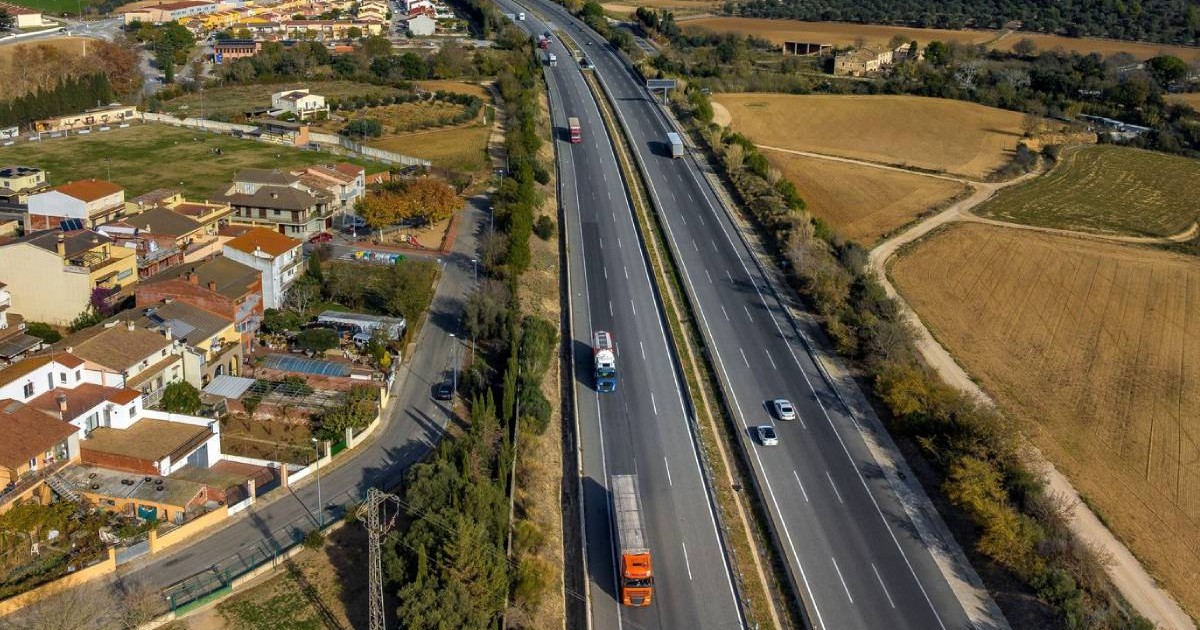 Vedere aeriană a autostrăzii AP-7 la trecerea ei pe lângă orașul Vilafant, Girona, Catalonia, Spania, decembrie, se vad masini si camioane, locuinte si terenuri