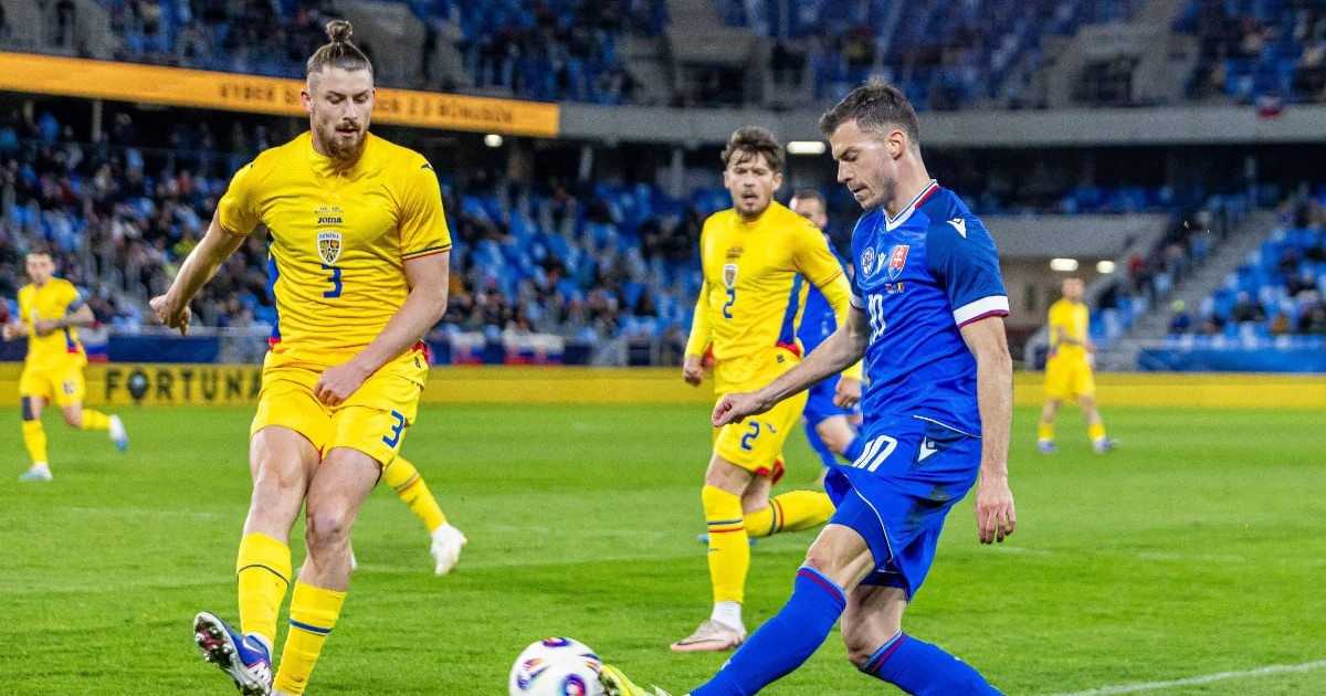 Doi jucători de fotbal se luptă pentru minge în timpul unui meci disputat pe stadion, unul dintre ei pregătindu-se să șuteze. În fundal, alți jucători și tribunele pline completează atmosfera intensă a partidei.