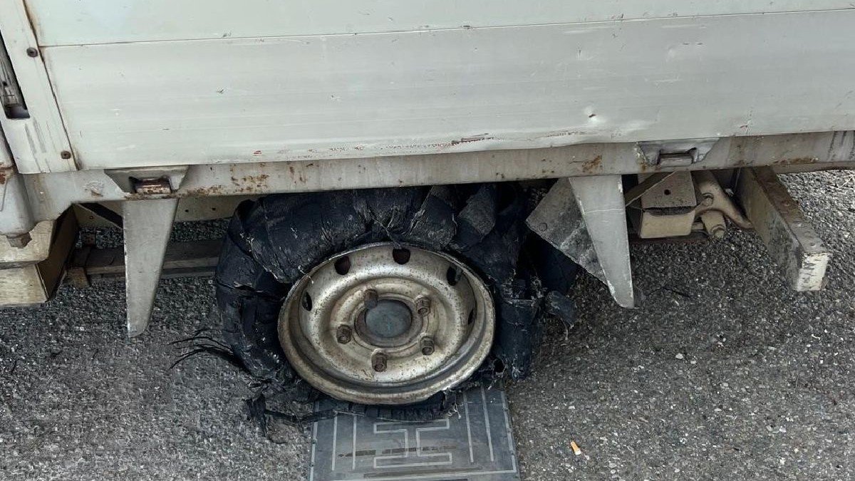 Prim-plan al unui pneu explodat de pe un vehicul alb, așezat pe o suprafață de beton cu urme vizibile de deteriorare