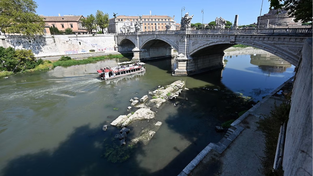O barcă turistică trece pe lângă un pod roman antic care iese din râul Tiber, în centrul Romei, pe 13 august 2026.