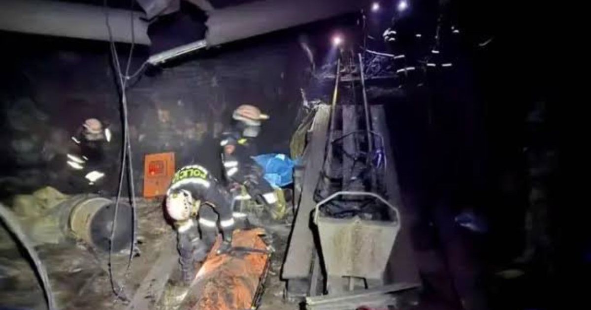 Imagini intunecate din interiorul unei mine cu doi asalvatori, unul in picioare si unul aplecat, mai multi scripeti in jur si lumina de la lanterne