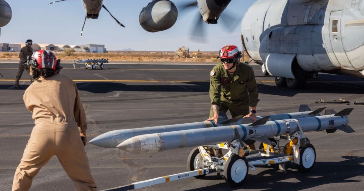 Rachete aer-aer avansate cu rază medie de acțiune AIM-120, împinse pe o pistă de aeroport de doi sergenți americani.