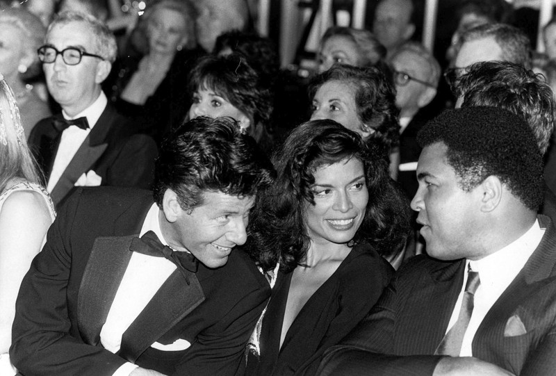 În momentul aventurii cu Rae, Mick Jagger era însurat cu Bianca Jagger - aici, între Calvin Klein și Muhammad Ali