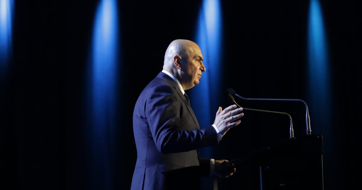 Ilie Bolojan, în timpul Congresului PNL, vorbește de pe scenă și se adresează participanților, are o mână ridicată cu care gesticulează