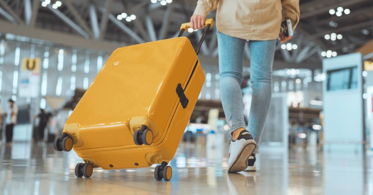 persoana care trage un troler portocaliu intr-un aeroport