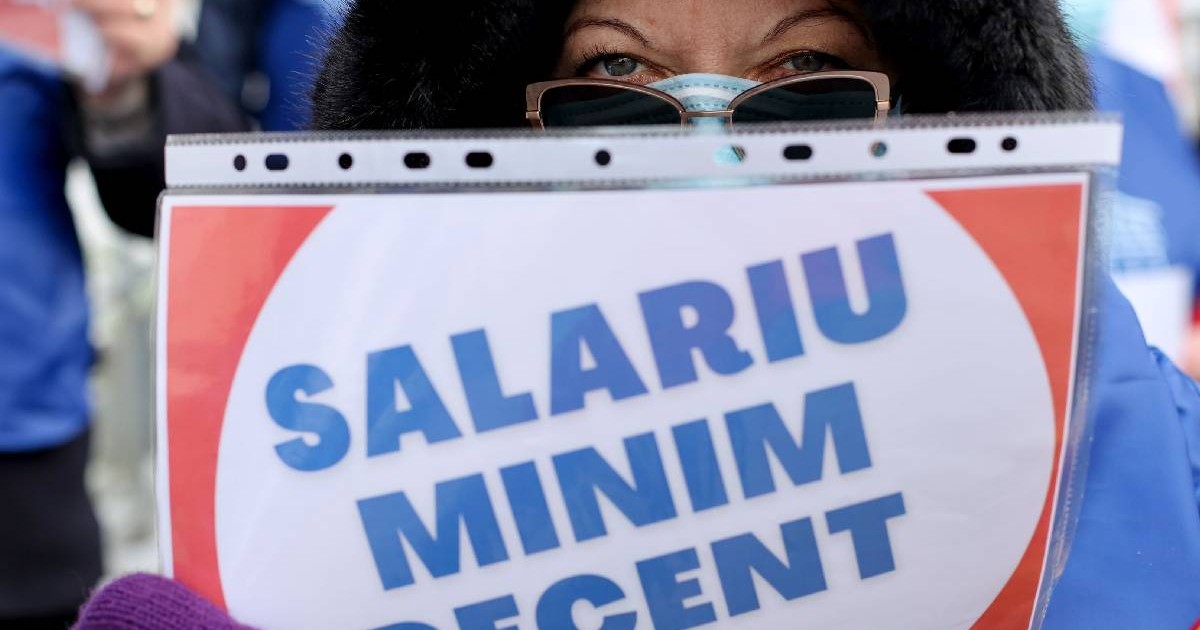 o femeie șine în mână o pancartă pe care scrie salariu minim decent