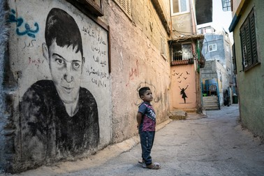 Pe o stradă din tăbăra de refugiați Aida din Betleem, un copil stă lângă un graffiti care amintește de victimele conflictelor dintre israelieni și palestinieni