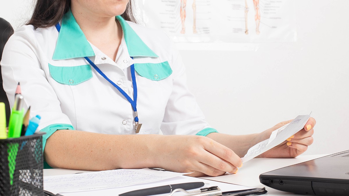 O doctoriță ține în mână un certificat de concediu medical în cabinetul unui centru medical. Conceptul de acordare a concediului medical de către medic
