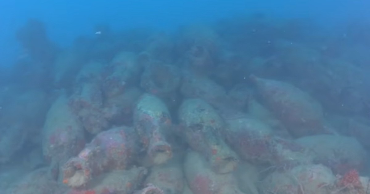 Imaginea surprinde, sub apă, un vas antic scufundat, acoperit parțial de sedimente și depuneri marine. Printre rămășițele epavei se disting numeroase amfore, păstrate în mare parte în poziția lor originală.