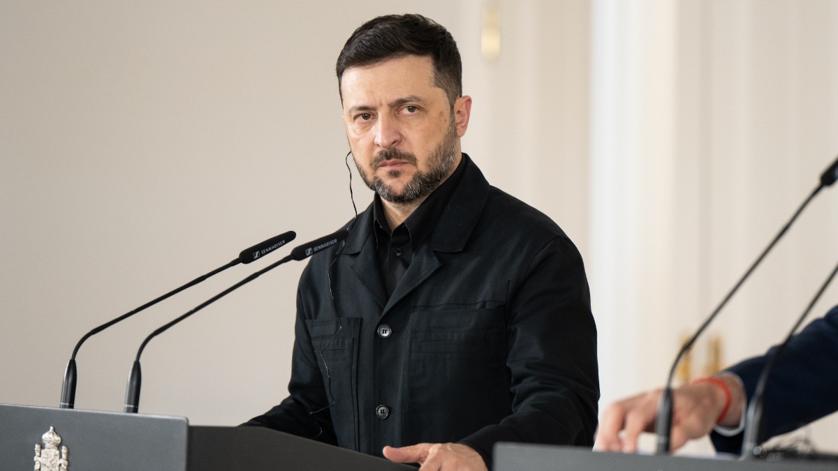 Bărbatul se află la un pupitru oficial, în fața mai multor microfoane, având o expresie serioasă și concentrată. Contextul și decorul sugerează o declarație publică sau o conferință de presă într-un cadru instituțional.