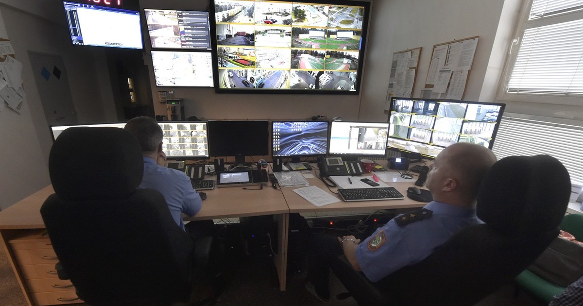 doi politisti aflati intr-o cameră de control monitorizeaza imaginile de pe ecran primite de la camerel video din oras