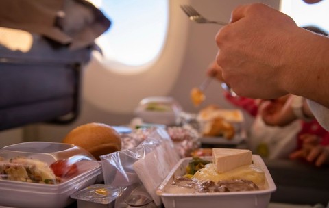 pasager dintr-un avion care savurează o masă caldă la bord, pe o masă pliantă