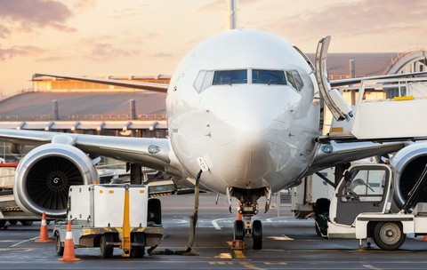 Un avion comercial alb staționează pe pistă, pregătit pentru îmbarcare, cu scara de îmbarcare desfășurată până la ușă