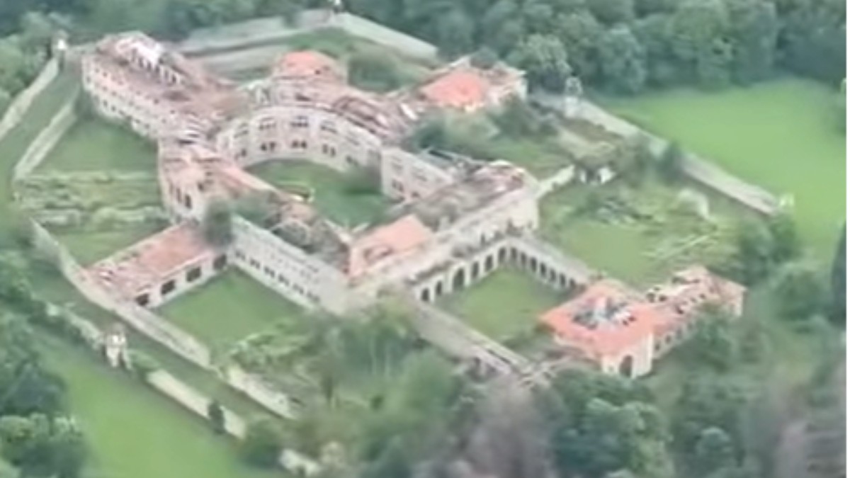 Imaginea surprinde o vedere aeriană a unui complex arhitectural de mari dimensiuni, înconjurat de ziduri și spații verzi, cu o curte interioară de formă circulară. Clădirea are acoperișuri din țiglă și este amplasată într-o zonă împădurită, ceea ce evidențiază amploarea și poziționarea izolată a ansamblului.