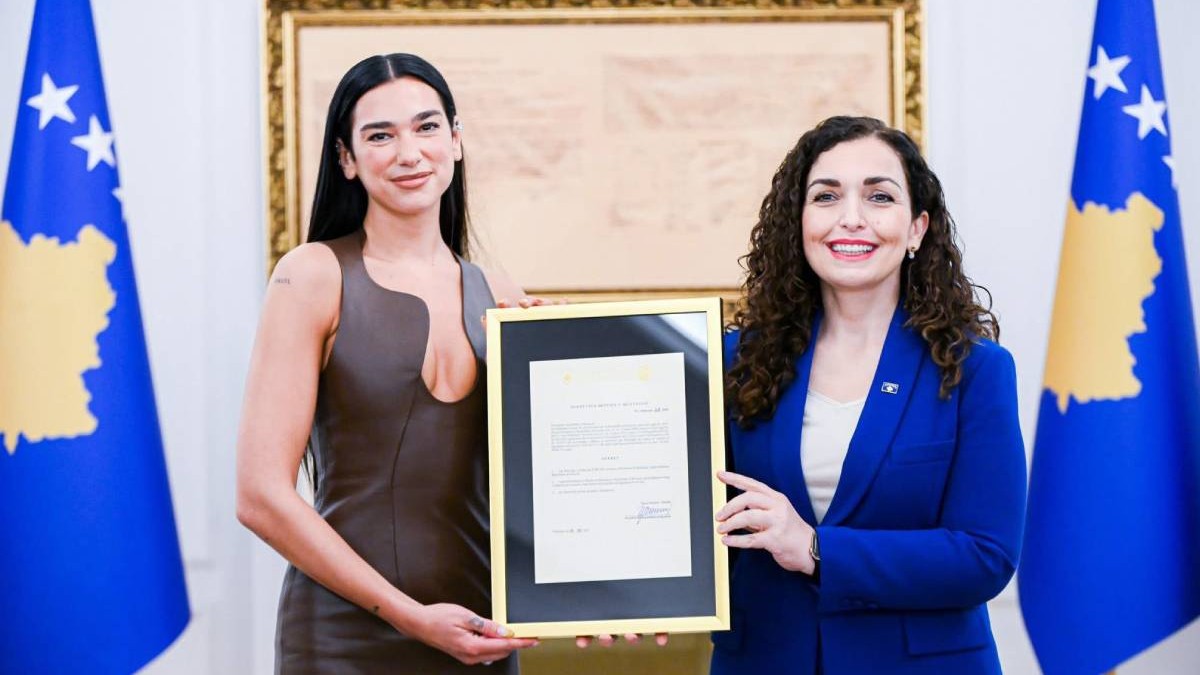 Imagine cu Dua Lipa (stânga) și Vjosa Osmani (dreapta) în timpul ceremoniei de acordare a cetățeniei kosovare. Cântăreața poartă o rochie maro cu decolteu