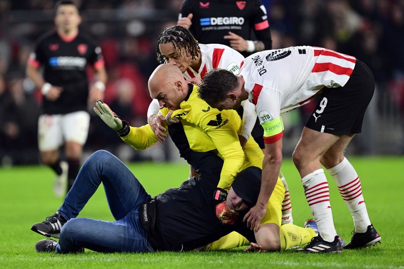 epa10486473 A pitch invader assaults Sevilla FC goalkeeper Marko Dmitrovic during the UEFA Europa league play-off soccer match between PSV Eindhoven and Sevilla FC, in Eindhoven, Netherlands, 23 February 2023. EPA-EFE/OLAF KRAAK